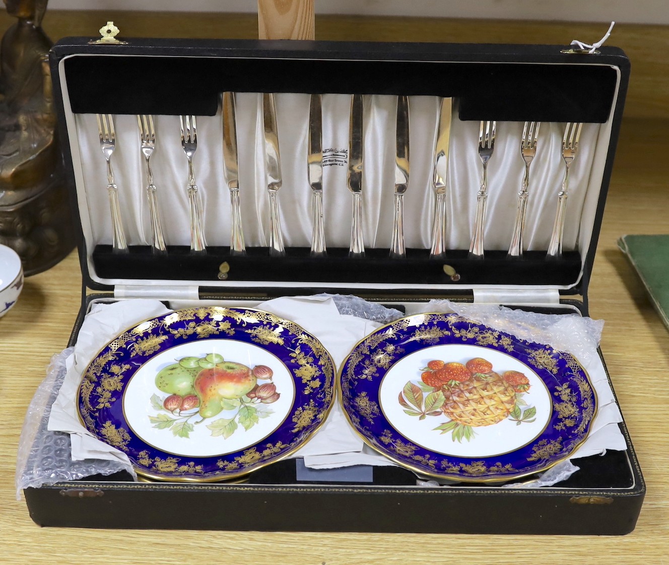 A cased dessert service containing six gilt and fruit decorated plates and a set of knives and forks